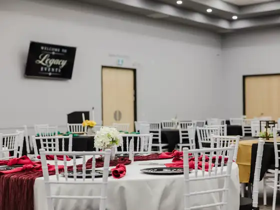Ballroom tables set with red linens beneath a Legacy Events welcome screen